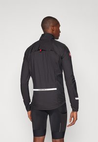 Schwarze Radjacke aus leichtem, wasserabweisendem Material. Verfügt über einen hohen Kragen, reflektierende Details und ein Logo in Taillenhöhe.