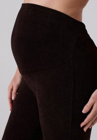 Dunkelbraune Corduroy-Leggings mit einem hohen Bund, die eine weiche Textur und eine schlanke Passform aufweisen. Seitennähte sind in der Hüftgegend sichtbar.