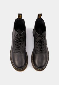 Botas de cuero negro hasta el tobillo con punta redonda, cordones en la parte delantera y costuras amarillas a lo largo de la suela. Presenta una lengüeta en el talón.