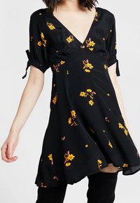 Svart blommigt klänning med v-ringning, korta puffärmar och draperade detaljer. Har en flödande silhuett med gula och rosa blommönster.