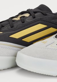 Schwarze und graue Sneakers mit gelben Akzenten, einer strukturierten Oberfläche und einer durchsichtigen Gummisohle mit glatter Oberfläche.