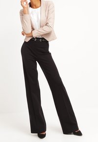 Lichtbeige getailleerde jas, witte blouse, hooggekraagde zwarte broek en zwarte hakken, met een slank ontwerp en een perfect afgestemde pasvorm.