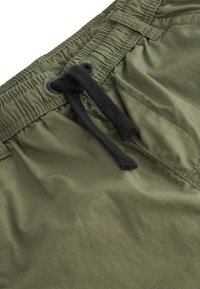 Shorts verts en tissu léger avec une taille élastique, un cordon noir et des détails cousus pour la structure.
