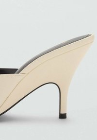 Zapato de tacón alto beige con una parte superior suave y texturizada, forma cónica y suela negra contrastante. Presenta un diseño minimalista sin embellishments.