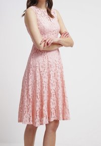 Růžové krajkové šaty s bezramínkovým, upnutým živůtkem a rozšířenou sukní. Květinový vzor po celém obvodu, hladká textura a délka ke kolenům.