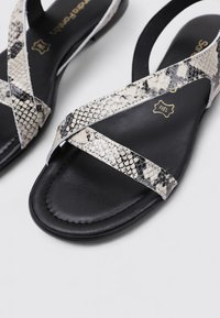Sandales noires avec un design de sangle en faux serpent. La partie supérieure présente un motif entrecroisé, tandis que la semelle est lisse et plate.