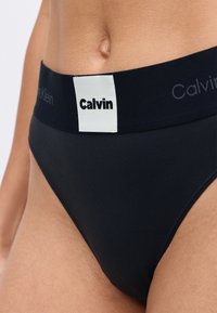 Svart bomullsbikini med bred elastisk linning som har en logo-patch og tekstdetaljer. Glatt tekstur med klassisk snitt.