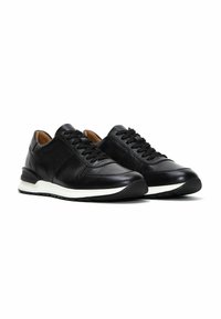 Zapatillas de piel negra con superficie texturizada, cordones planos y una suela de goma blanca. Presentan costuras sutiles y un talón acolchado.