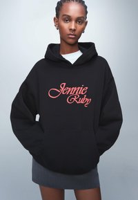 Felpa nera con cappuccio e "Jennie Ruby" in scrittura rossa sul davanti. Il materiale sembra morbido, presenta una tasca frontale e una vestibilità comoda.