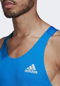 Débardeur de sport bleu en tissu lisse, avec un col rond et un logo Adidas blanc sur le côté gauche à l'avant.