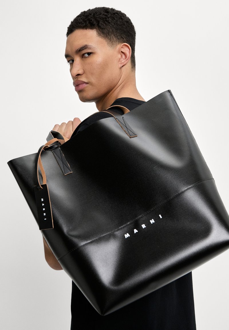 Borsa tote nera realizzata in materiale morbido, con manici in pelle beige e un logo bianco prominente "MARNI" sulla parte anteriore.