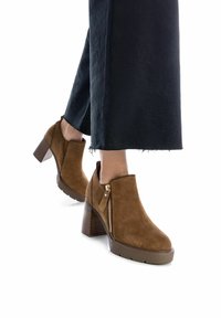 Stivaletti alla caviglia in suede marrone con tacco largo e zip laterale. La suola texturizzata e le linee pulite esaltano il design moderno e casual.