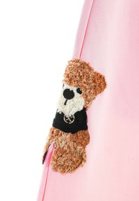 Bolsa de tela rosa con un parche de oso de peluche difuso y texturizado en marrón, negro y blanco, que presenta un emblema redondo en la parte superior negra del oso.