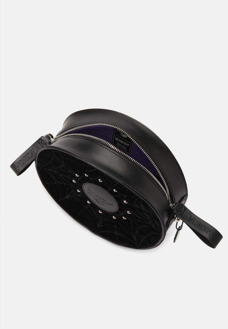 Schwarze runde Tasche mit einem strukturierten Samt-Spinnennetzdesign, silbernen Reißverschlüssen und einem Ledergriff, der mit "WEDNESDAY" beschriftet ist. Innenfutter in tiefem Lila.