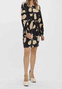 Černé šaty s béžovým abstraktním vzorem, dlouhými nabíranými rukávy, úzkým pasem a rovnou siluetou. Spárované s krémovými botami na blokovém podpatku.