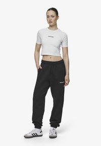 Tricou scurt alb cu un logo negru, asortat cu pantaloni de trening cu talie elastică negri. Modelul poartă pantofi sport gri și albi.