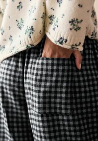 Virágmintás, krémszínű pulóver bordázott alsó résszel, szürke és fekete kockás nadrággal párosítva, elülső zsebével.