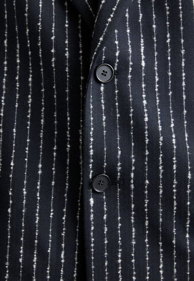 Ναυτικό πουκάμισο με λευκές κατακόρυφες ρίγες, φτιαγμένο από υφασμάτινη ύφη. Διαθέτει μαύρα κουμπιά και κλασικό σχέδιο γιακά.