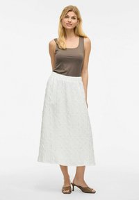 Brązowy top na ramiączkach i biała teksturowana spódnica midi z elastycznym paskiem w talii. Uzupełniona brązowymi sandałami na obcasie, prezentowana na neutralnym tle.