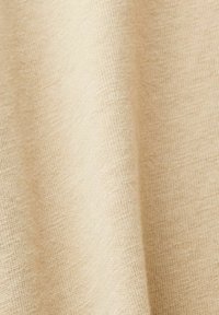 Tissu beige avec une texture douce et un motif tricot subtil, présenté dans une position drapée, mettant en avant sa surface lisse et ses fibres naturelles.