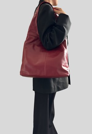 Borsa a spalla in pelle bordeaux con una texture morbida, leggero lucido e dettagli delle cuciture diagonali. Design spazioso sostenuto da una singola tracolla.