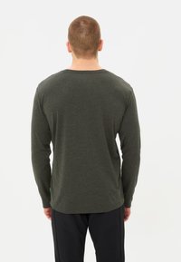 Maglietta verde a maniche lunghe realizzata in tessuto morbido con scollo rotondo, caratterizzata da un orlo curvo e dettagli della cucitura sul retro. Design semplice senza motivi.