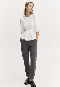 Vit, strukturerad blus med smockad midja, tillsammans med skräddarsydda gråbyxor. Svarta skor fulländar outfiten och betonar en minimalistisk stil.