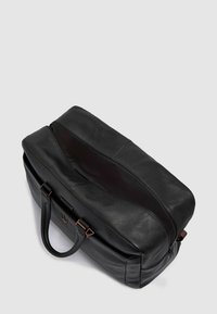 Sac de voyage en cuir noir avec surface texturée, double poignée et ouverture zippée. Comprend des accents en bronze sur la quincaillerie. Intérieur spacieux.