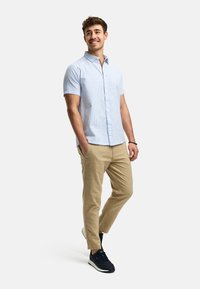 Korte mouwen blauwe gingham blouse gecombineerd met beige broeken en marineblauwe sneakers, met een button-down kraag en zijzakken.