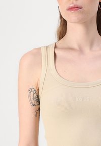 Beige ribbattu toppi, jossa on pyöreä pääntie ja brodeerattu "BOSS"-logo. Ominaisuutena on istuva muotoilu ja sileä tekstuuri.