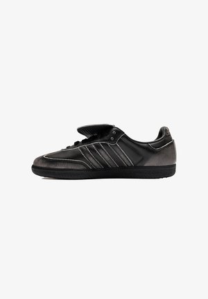 Scarpa da ginnastica nera low-top con tre dettagli laterali a strisce bianche e linguetta parzialmente aperta, mostrata di profilo su sfondo bianco.