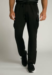 Zwarte joggingsbroek van glad materiaal, met een trekkoord in de taille en zijvakken voor opbergruimte. Accentueren met logo detail.