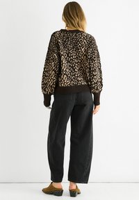 Leopard print sweater in brown and beige, featuring a relaxed fit and ribbed hem. Paired with high-waisted black jeans and brown clogs.