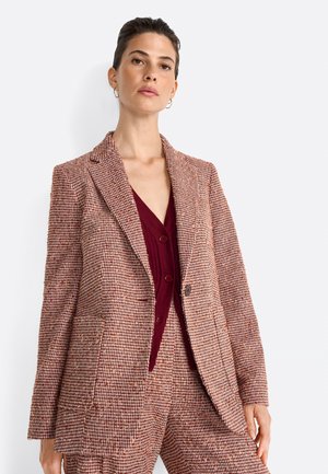 Blazer à carreaux marron et beige avec des revers en notch, deux poches avant et une coupe légèrement structurée, porté sur un top bordeaux profond.