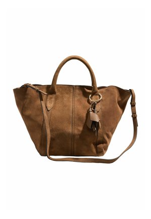 Brun ruskindshåndtaske med dobbelthanke, aftagelig skulderrem og dekorativ læderkvast som nøglering på hvid baggrund.