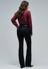 Jeans negros acampanados con cintura alta y bolsillos traseros, combinados con una camisa de satén burdeos con puños abotonados. Textura suave.