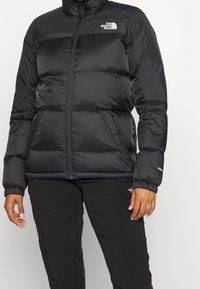 Doudoune noire avec un col haut, fermeture éclair et poignets élastiques. Présente une surface texturée et le logo The North Face sur la poitrine.