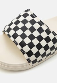 Black and white checkered slide sandal with a synthetic upper, featuring a wide strap and a textured beige footbed. Stitched detailing is visible.