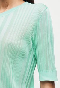 Πλεκτό τοπ σε μέντα πράσινο με κάθετες ρίγες, κοντά μανίκια με ραμμένο τελείωμα και υφή ελαφριού υφάσματος.