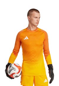 Maglia da portiere a maniche lunghe arancione con motivo a onde, guanti neri e un pallone da calcio rosso e bianco. Logo Adidas su maglietta e pantaloncini.