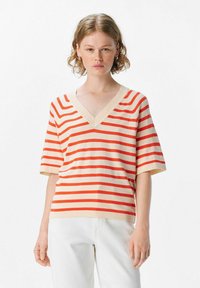Striped short-sleeve V-neck sweater in cream with bold red stripes. Features a relaxed fit and ribbed neckline. Textured knit fabric.