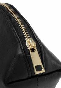 Funda de cuero negro con un zipper dorado. Presenta un acabado texturizado y una forma triangular, destacando elementos de diseño modernos y elegantes.