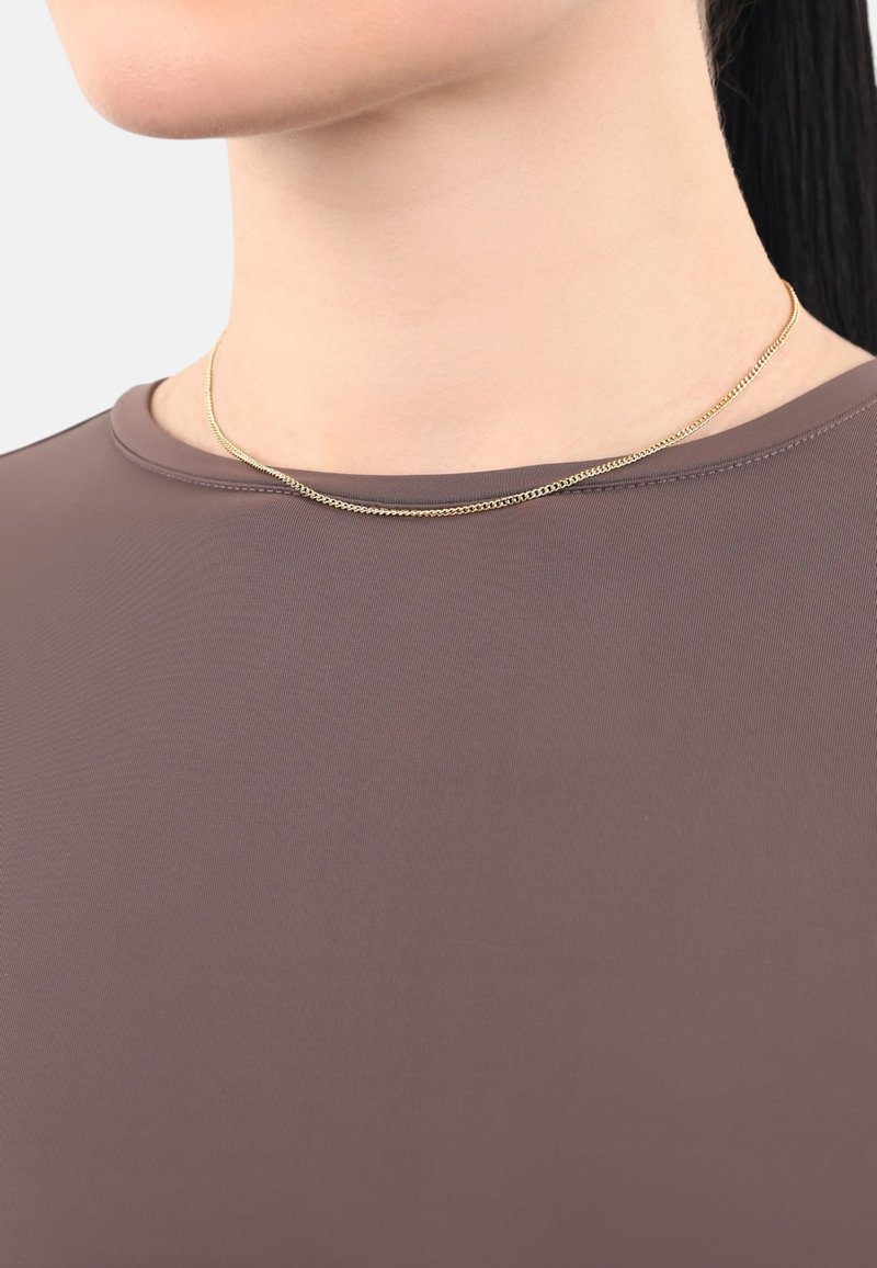 Un collar de cadena de oro reposa sobre un escote redondeado de una blusa ajustada y suave en tono malva. La blusa tiene un ligero brillo y un diseño minimalista.