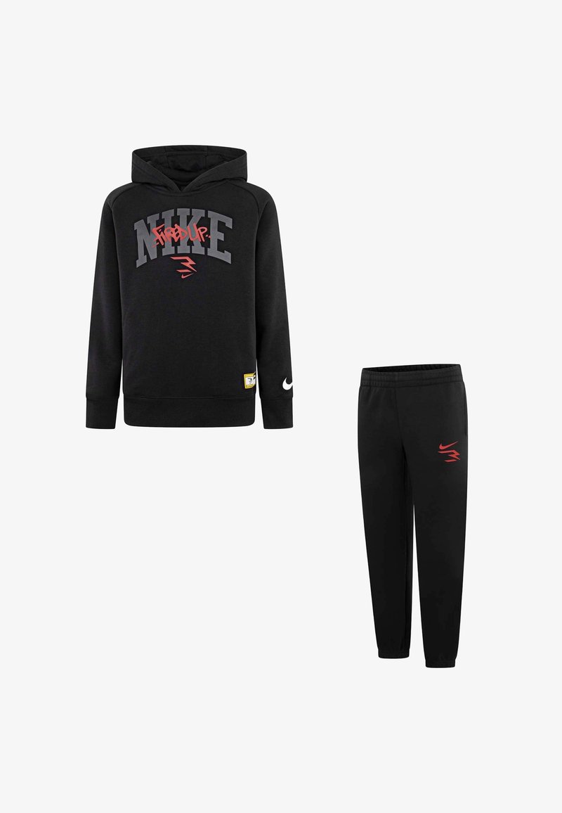 Felpa Nike nera con grafica "fired up" e pantaloni tuta neri abbinati con logo rosso sulla coscia sinistra.