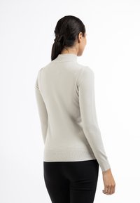 Pulover cu guler înalt, de culoare gri deschis, cu mânecă lungă și un design ajustat. Textură moale, manșete și tiv rêbinate. Purtați cu pantaloni negri.