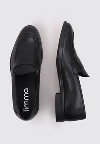 Mocasines de cuero negro con suela plana, punta redondeada y una correa decorativa en la parte frontal. Textura suave, detalles de costura mínimos.
