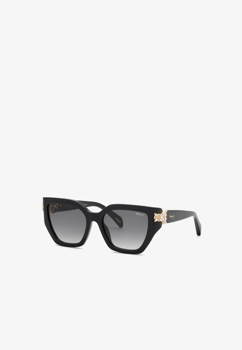 Lunettes de soleil oversize noires en forme d'œil de chat avec des verres dégradés et des ornements floraux dorés sur les branches.
