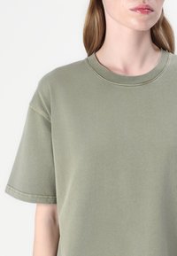 Olive green cotton t-shirt with a round neckline and short sleeves. Features a soft texture and visible stitching along the seams.