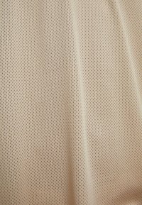 Perforert stoff i en lys beige farge, med jevnt fordelte hull. Teksturen virker myk og fleksibel, noe som gir god pusteevne.