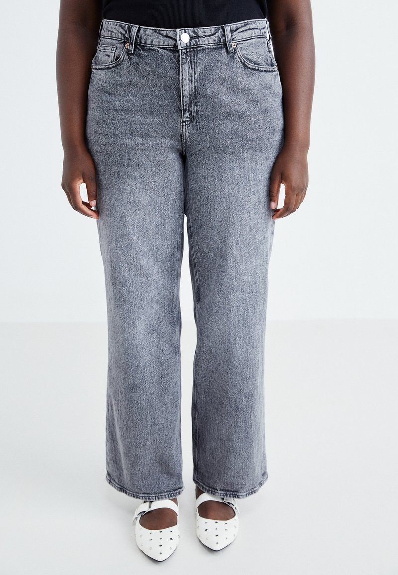 High-waisted, gray denim jeans with a relaxed fit, five pockets, and a button closure, paired with white dotted flats.